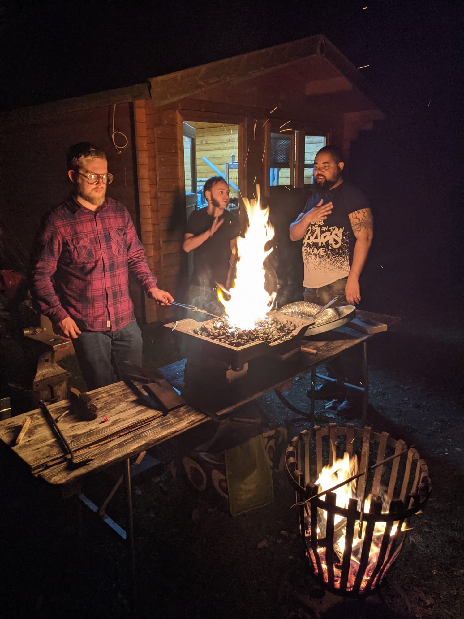 Blacksmiths gathered around a glowing outdoor forge at night in Germany